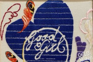 Das Bild zeigt ein besticktes Handtuch mit einem blauen Herz und dem Schriftzug "Good Girl" als Bildmetapher für die eigene Definition von Erfolg (Photocredit: Petra Welz, Geld & Rosen, Düsseldorf)