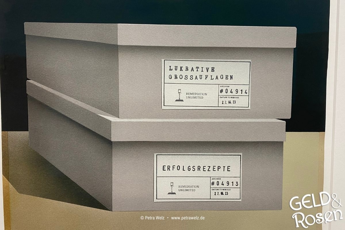 Das Bild zeigt zwei übereinandergestapelte Pappschachteln mit der Aufschrift "Lukrative Großauflagen" und "Erfolgsrezepte" – Analogie zur Unternehmensnachfolge und Übergabe in Teams (Photocredit: Petra Welz, Geld & Rosen, Düsseldorf).
